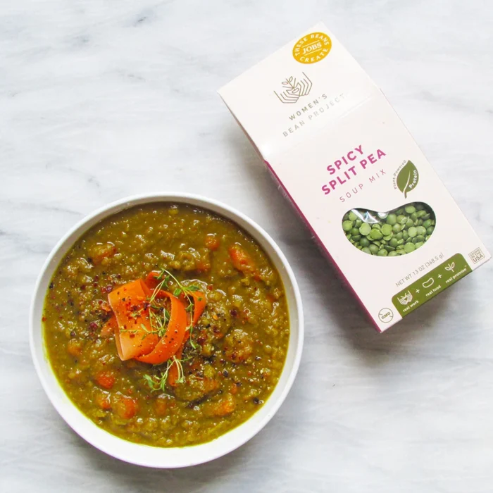 Women's Bean Project Spicy Split Pea soup mix laid on a table next to a bowl of the prepared soup