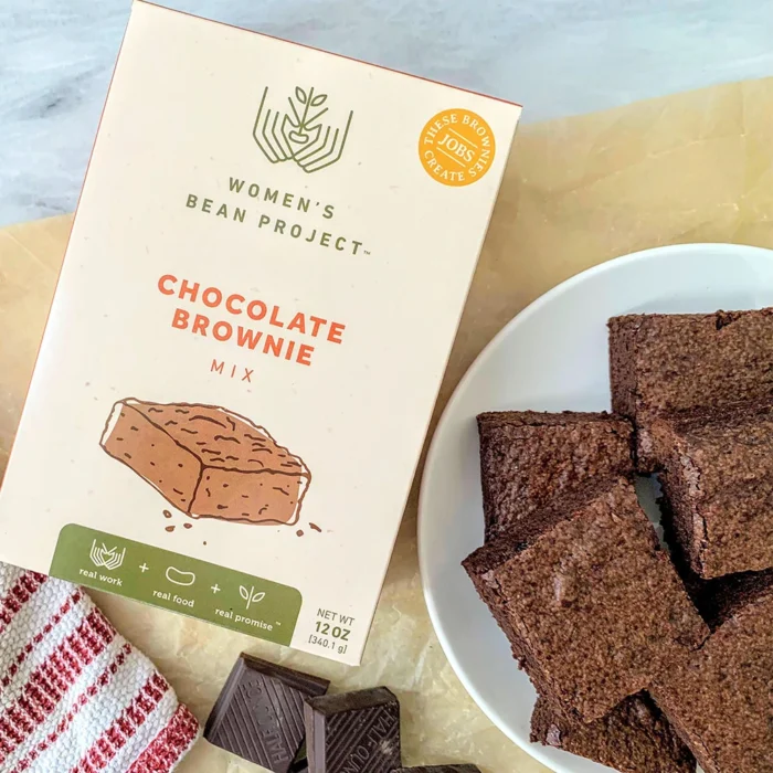 Women's Bean Project chocolate brownie mix laid on a table next to a plate of decadent brownies.