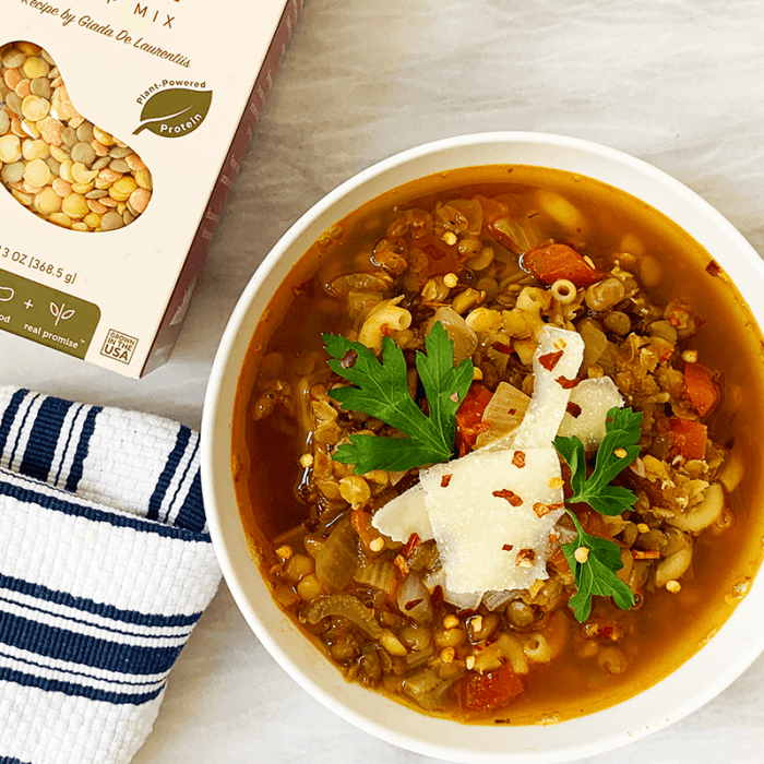 A Women's Bean Project Lentil Soup box next to a prepared bowl of lentil soup.