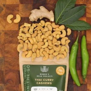 Women's Bean Project Thai Curry cashews being poured on a table with ginger, spices and peppers.