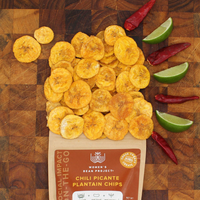 Women's Bean Project Chili Picante plaintain chips being poured onto a table with chilis and limes.