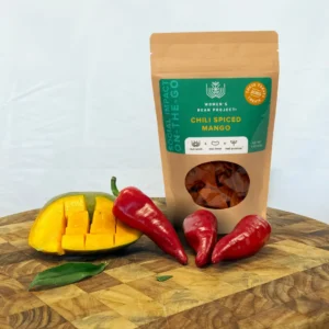 A bag of Women's Bean Project Chili Spiced Mango next to chilis and a fresh mango.