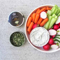 An open tin of Women's Bean Project Dill Spice Blend next to a plate of vegetables and dip.