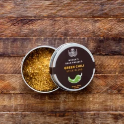 An open tin of Women's Bean Project Green Chili Spice Blend on a wooden table.