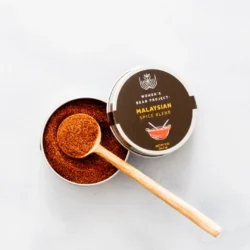 A wooden spoon in an open tin of Women's Bean Project Malaysian Spice Blend.